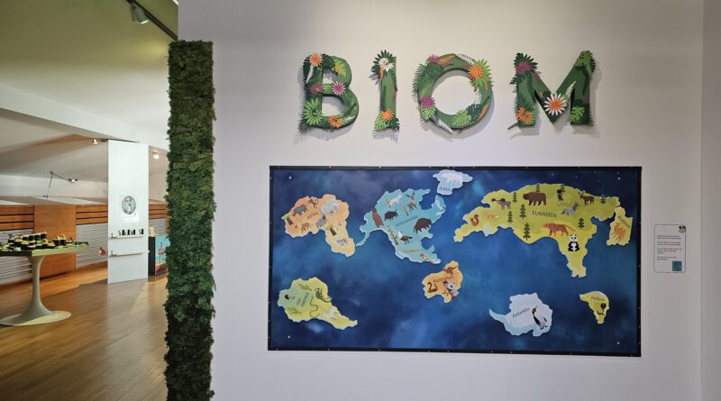 Der Eingang zur Ausstellung BIOM in der MEWO Kunsthalle: eine bunte Weltkarte mit Tieren und dem Schriftzug BIOM aus Pflanzen