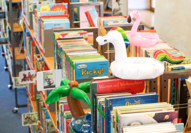 ein Regal voller Kinderbücher, darauf stehen kleine aufblasbare Schwimmfiguren