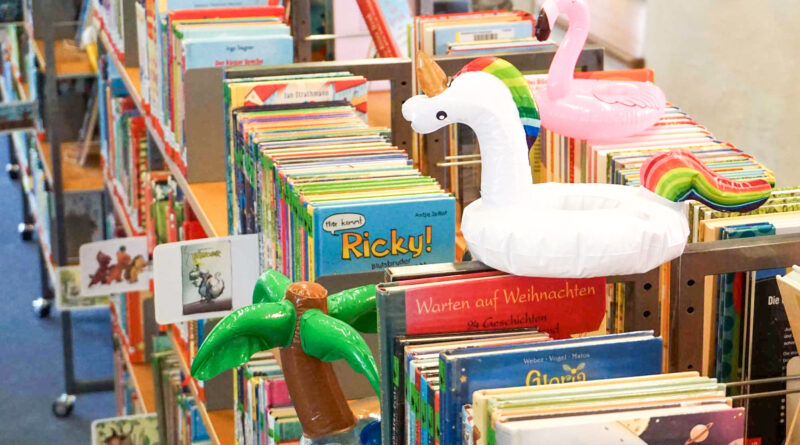 ein Regal voller Kinderbücher, darauf stehen kleine aufblasbare Schwimmfiguren