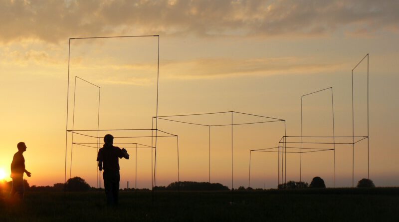 Personen vor einer Stahlskulptur von Hansjörg Beck auf einem Feld im Sonnenuntergang