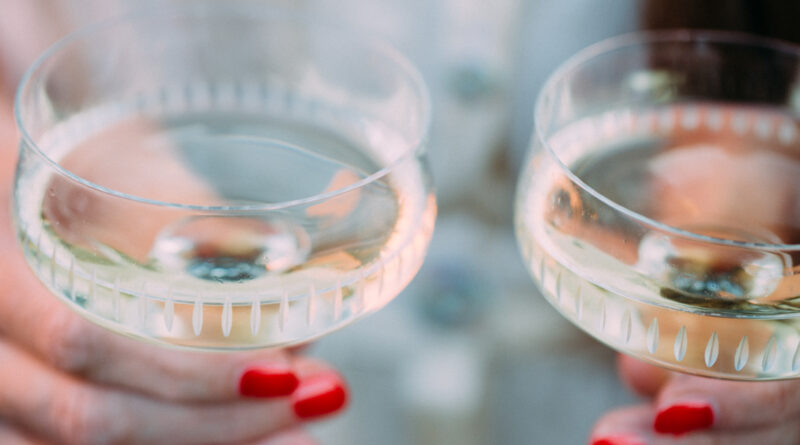 Nahaufnahme von zwei Händen mit rot lackierten Fingernägeln, die jeweils ein gefülltes Champagnerglas halten