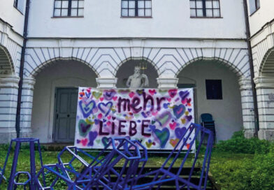 Ein Banner mit der bunten Aufschrift Mehr Liebe hängt im Innenhof des Hermansbaus