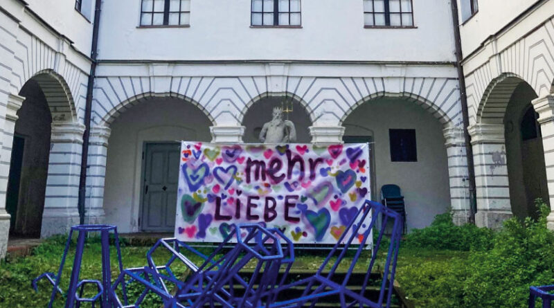 Ein Banner mit der bunten Aufschrift Mehr Liebe hängt im Innenhof des Hermansbaus