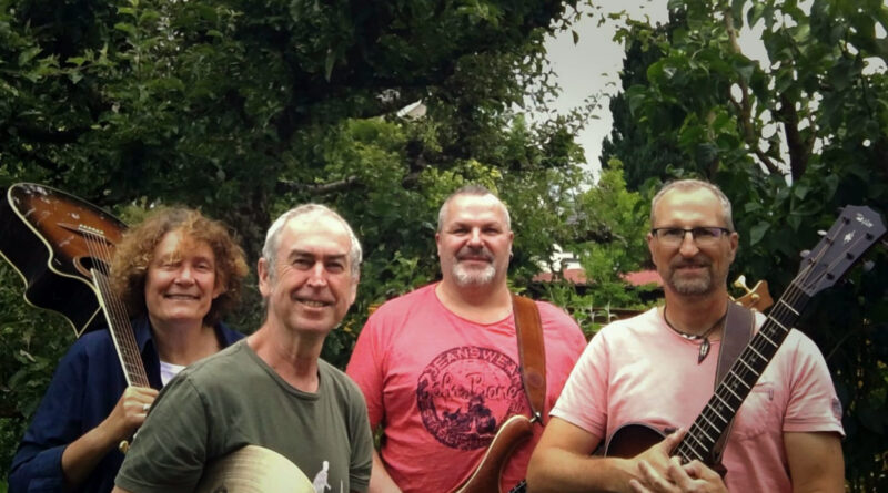 Die Mitglieder der Blue House Rockband mit ihren Instrumenten vor einer grünen Hecke