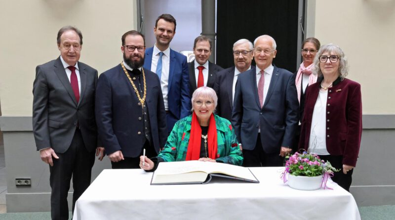 Staatsministerin Claudia Roth beim Eintrag ins Goldene Buch der Stadt. Dahinter stehen Vertreter der Stadt